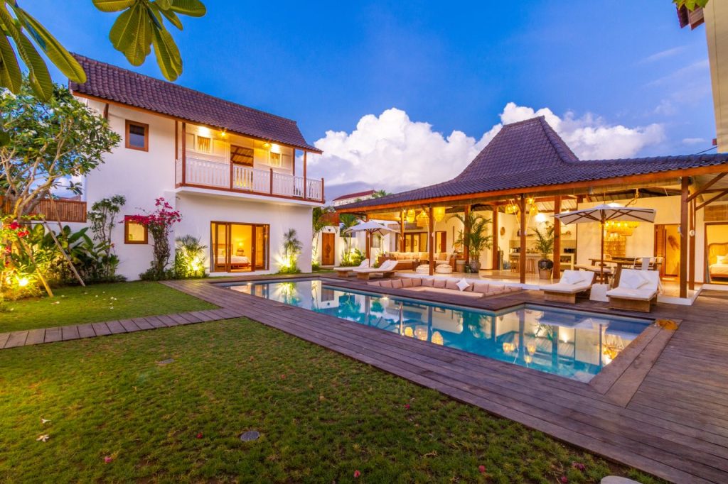 Stunning tropical villa exterior featuring a pool, wooden deck, and lush garden under a blue sky.
