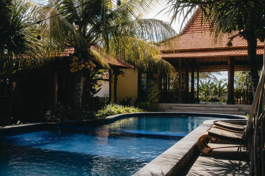Relax by a luxurious tropical pool surrounded by lush palm trees under a sunny sky, perfect for summer getaways.