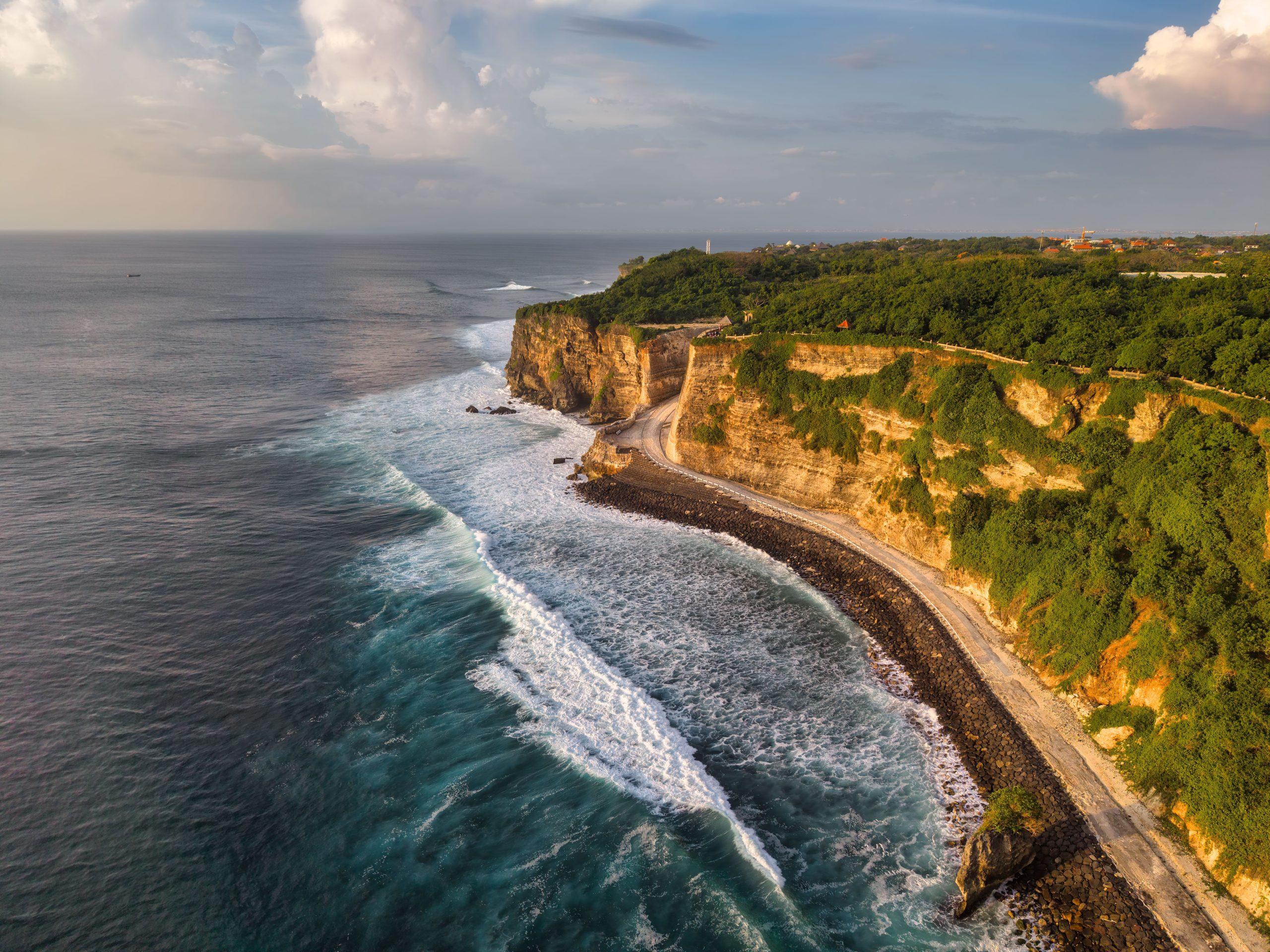 Breathtaking aerial view of Uluwatu cliffs and ocean waves in Bali, Indonesia during a sunny day.
